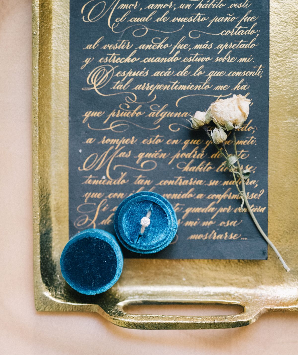 A close-up flat-lay of a gold eternity band next to a personalized handwritten love note and fresh flowers.