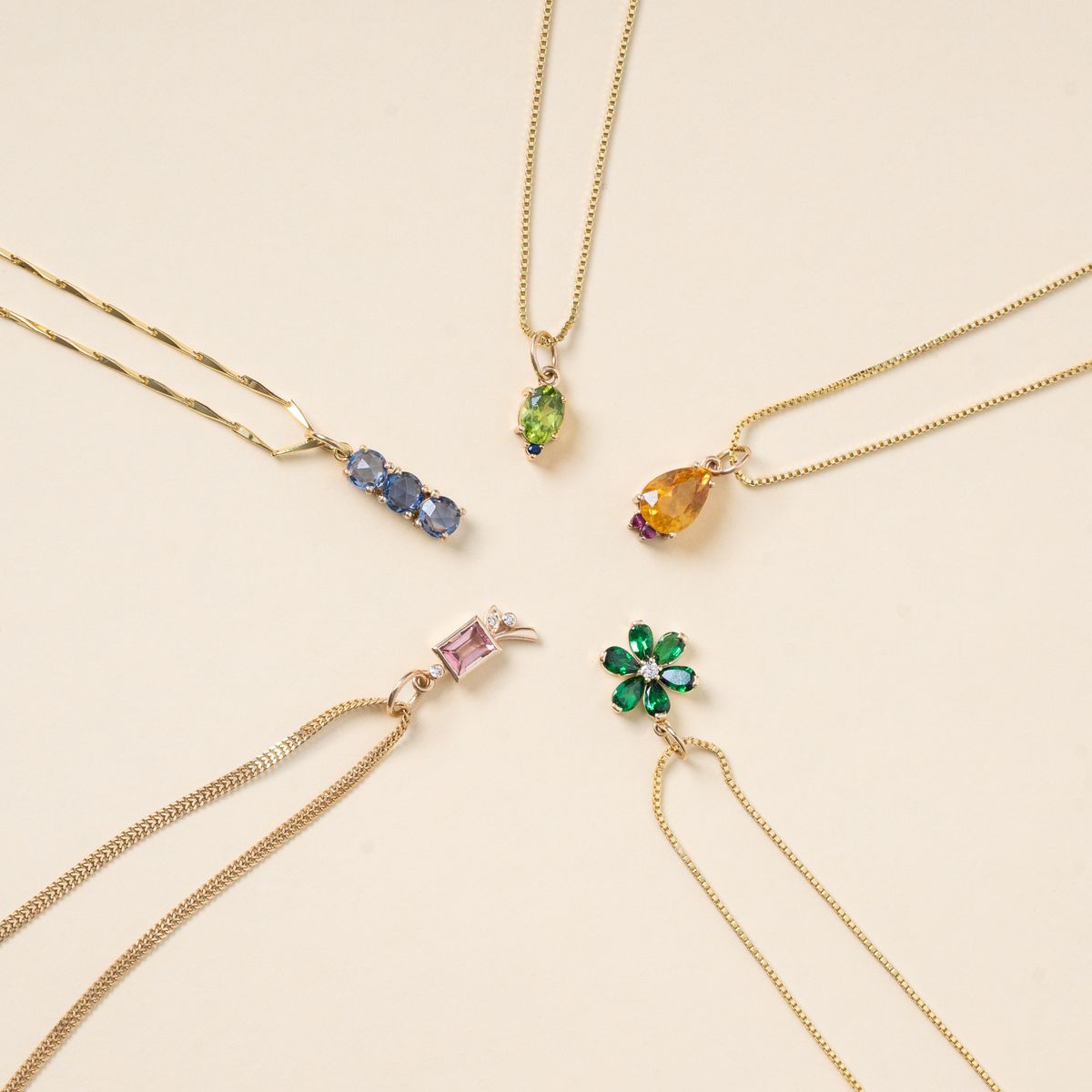 A flat-lay displaying colorful birthstone-inspired pendant necklaces arranged neatly in a circle.