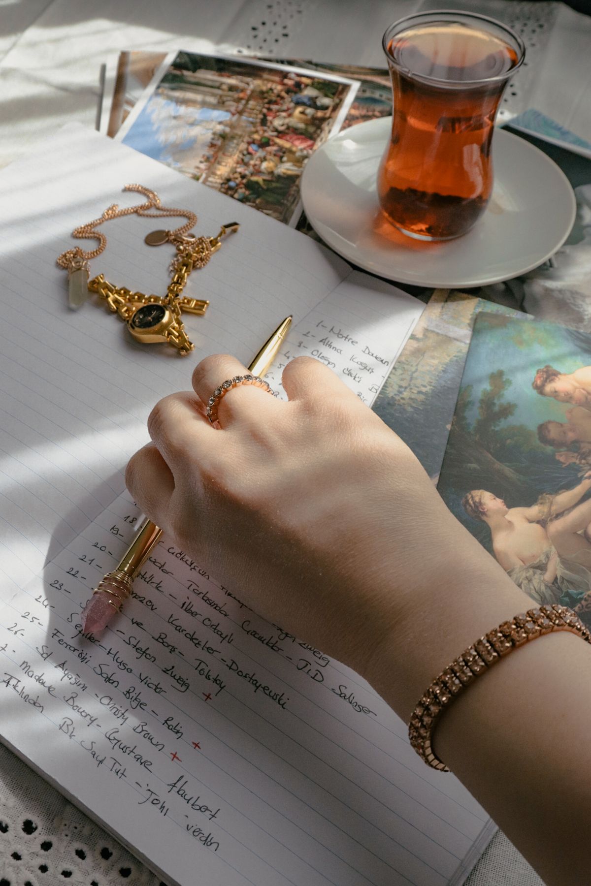 Hands adorned with stackable rings holding a fountain pen over a notebook.