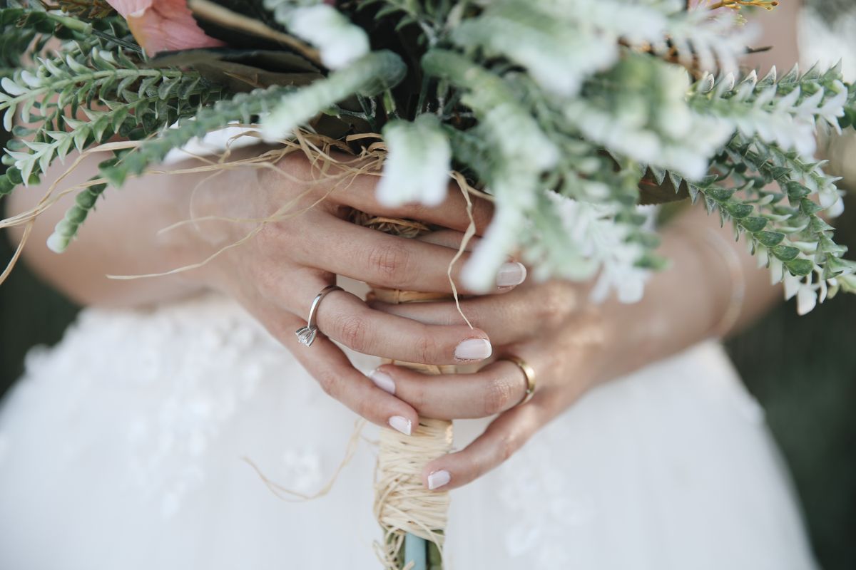 A bride's hands holding her bouquet, showing her wedding band and a delicate pearl bracelet.
