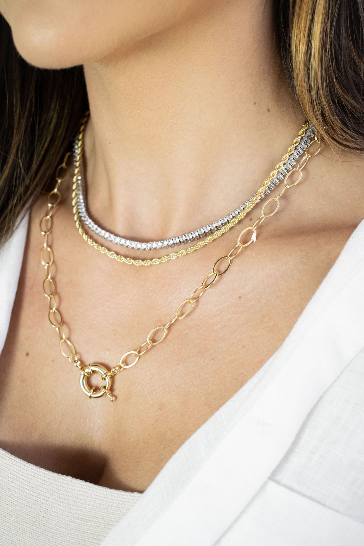 Combine a fine silver pendant chain with a warm gold choker — the metals rest closely together and appear curated.